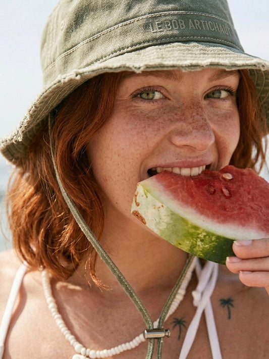 Femme rousse aux cheveux courts dégustant une pastèque sous le soleil en été.
